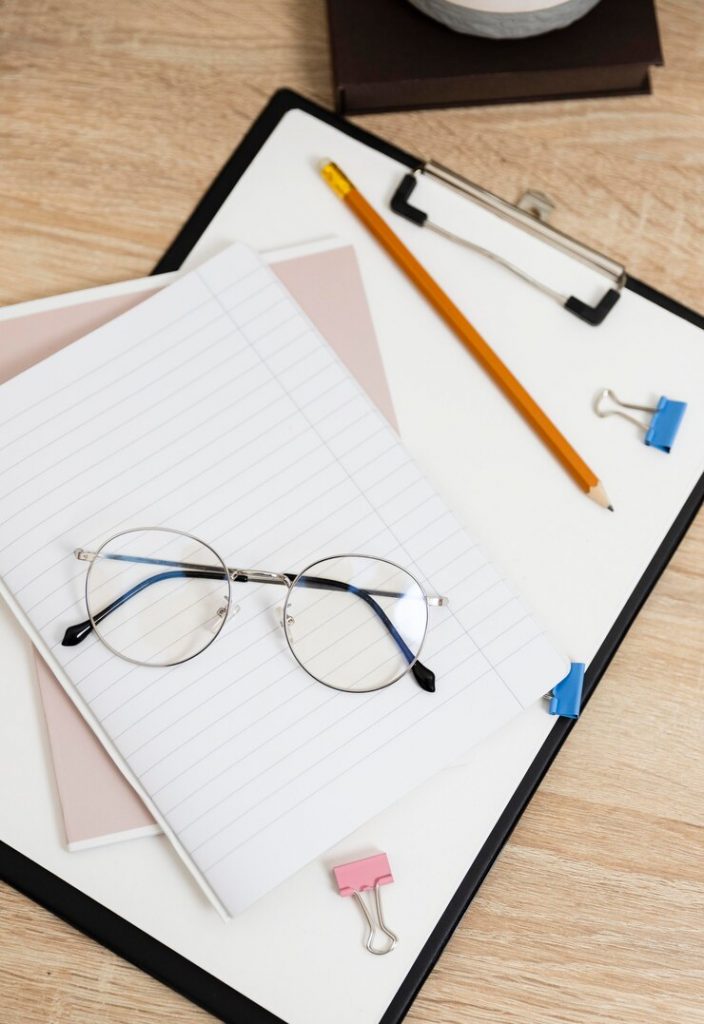a clipboard with papers and a pencil and a pair of glasses resting on top