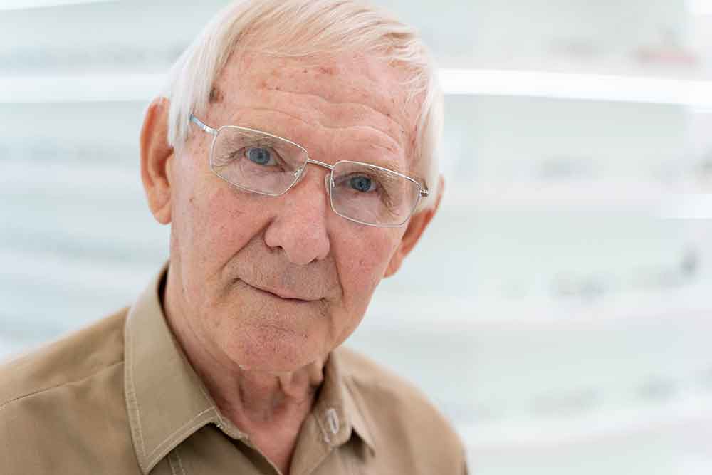 elderly man with glasses with blurred shelves in the background